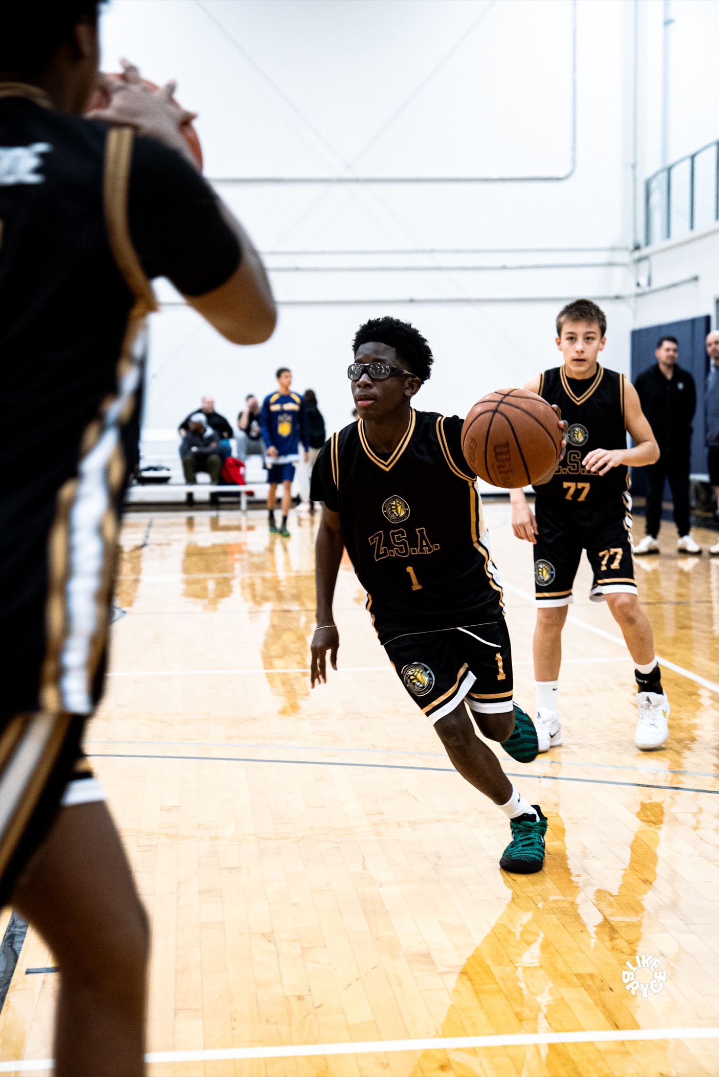 Young Zion player in a black ZSA jersey dribbling downcourt with a teammate behind him