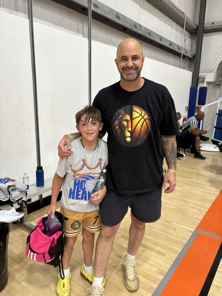 Coach in a lion-and-basketball shirt posing with a young player