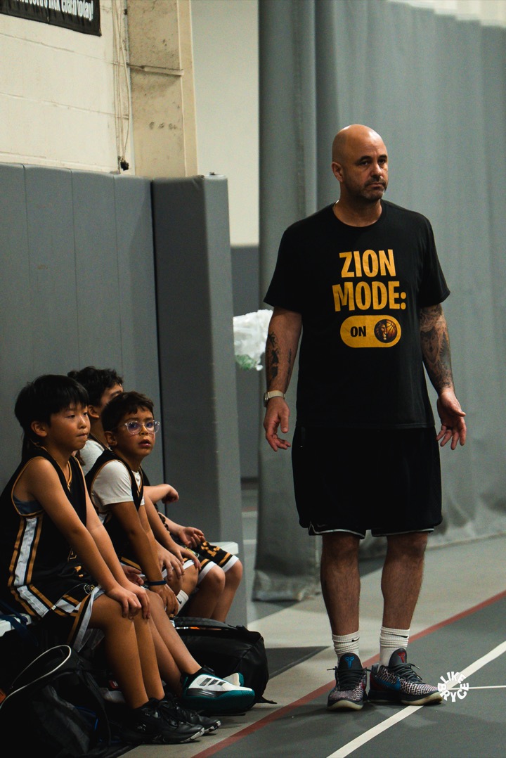 Coach in a black ZSA "Zion Mode" shirt standing by the team bench