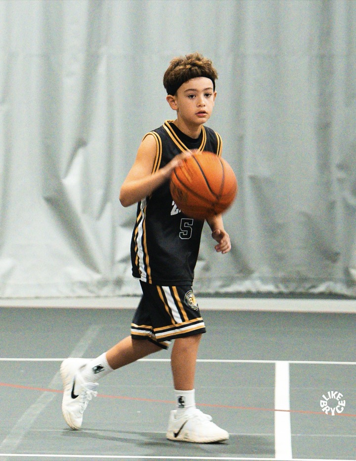 Young Zion player in a black ZSA jersey dribbling up the court