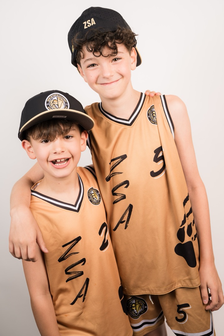 Two young athletes in gold ZSA jerseys and caps, smiling with their arms around each other