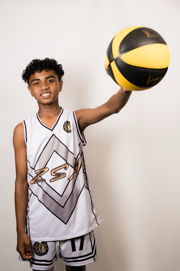 Young athlete in a white and silver ZSA jersey holding a basketball high